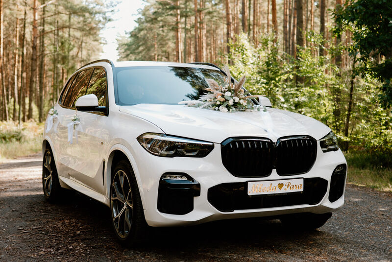 Białe BMW X5 przystrojone do ślubu na leśnej drodze